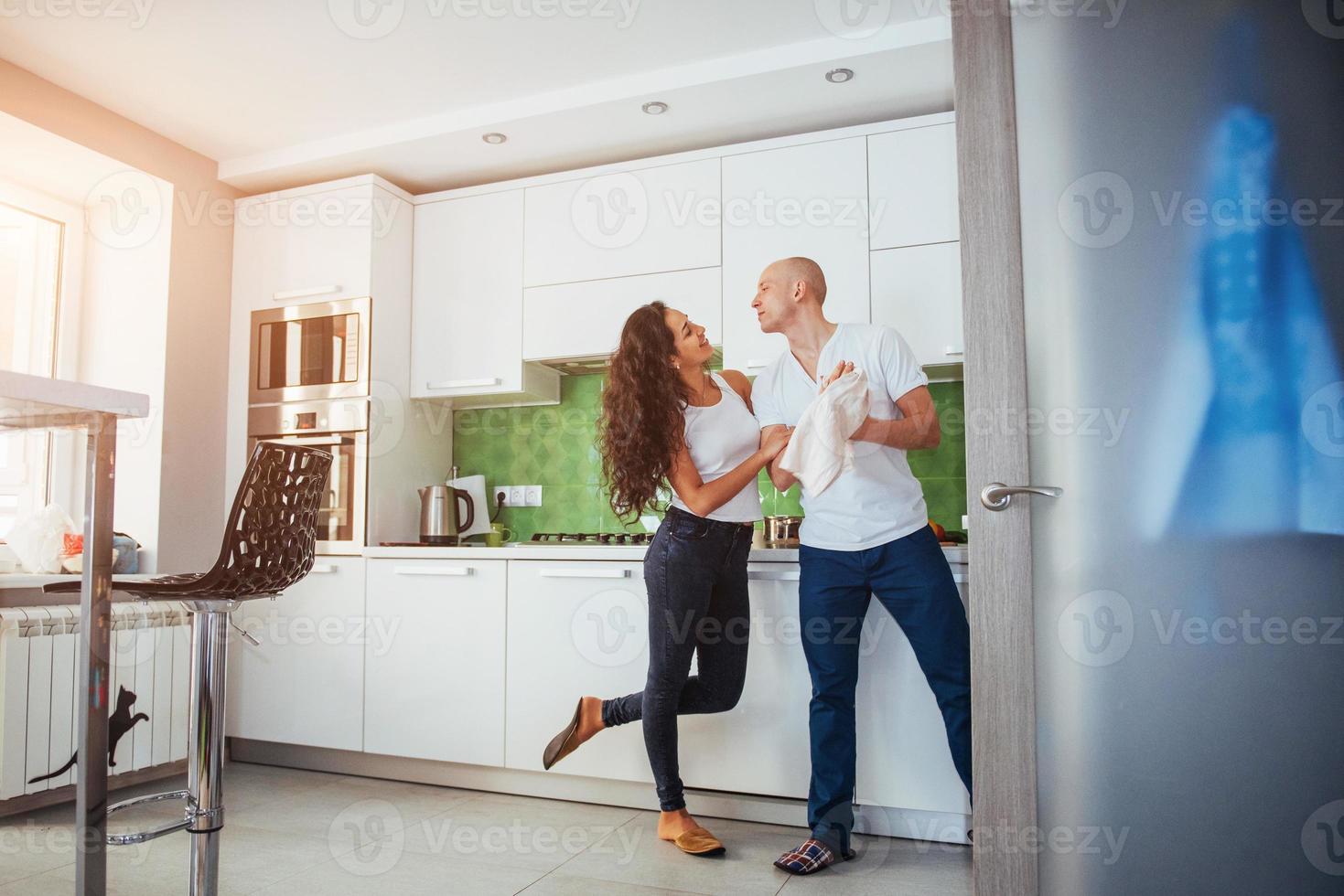 hermosa pareja joven está hablando, mirando a la cámara y sonriendo mientras cocina en la cocina. foto