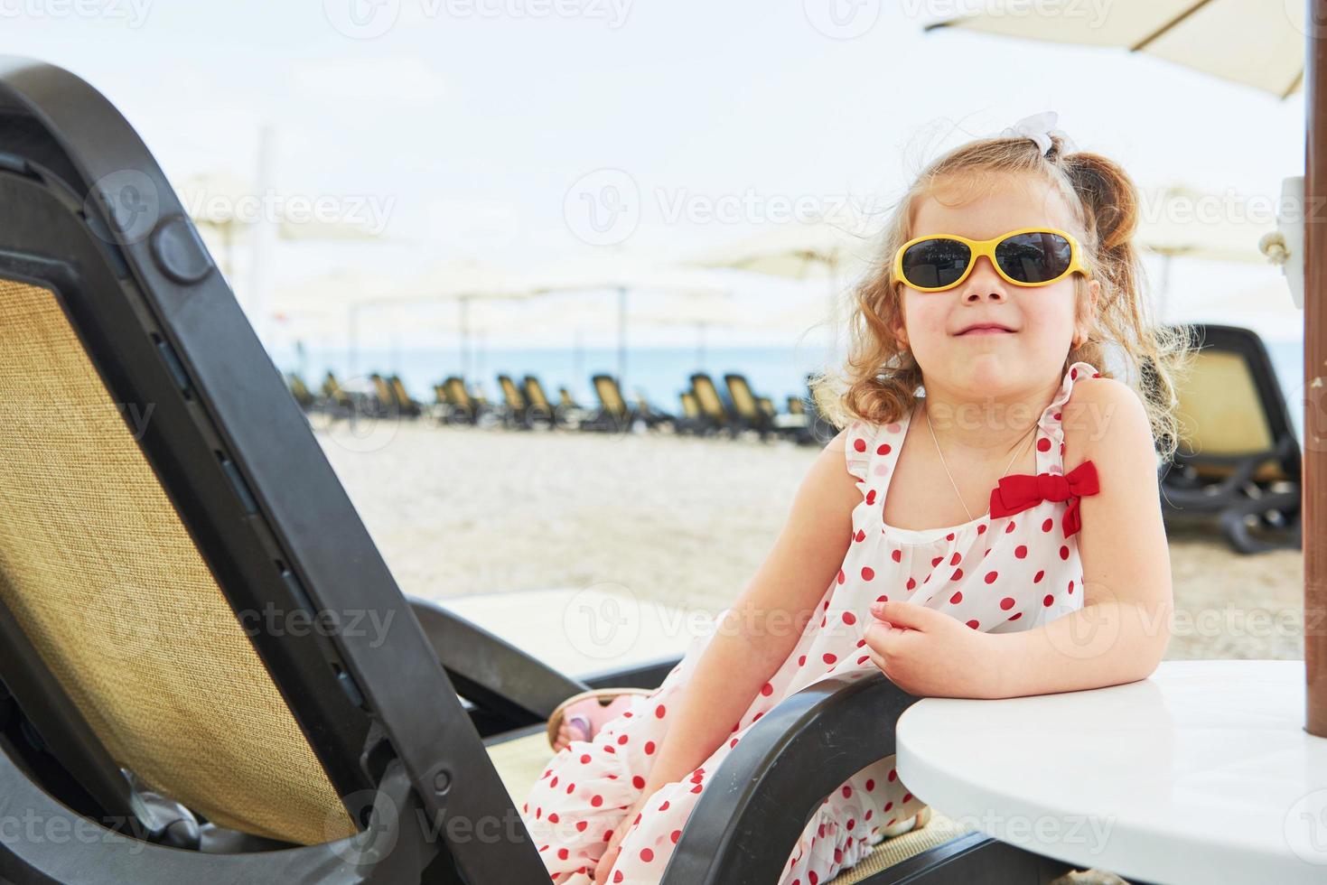 niña feliz en las tumbonas junto al mar, posando para la cámara foto