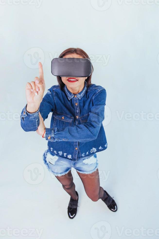 brunette beautiful woman posing in the studio, wearing jeans wear, using VR-glasses virtual reality headsets photo