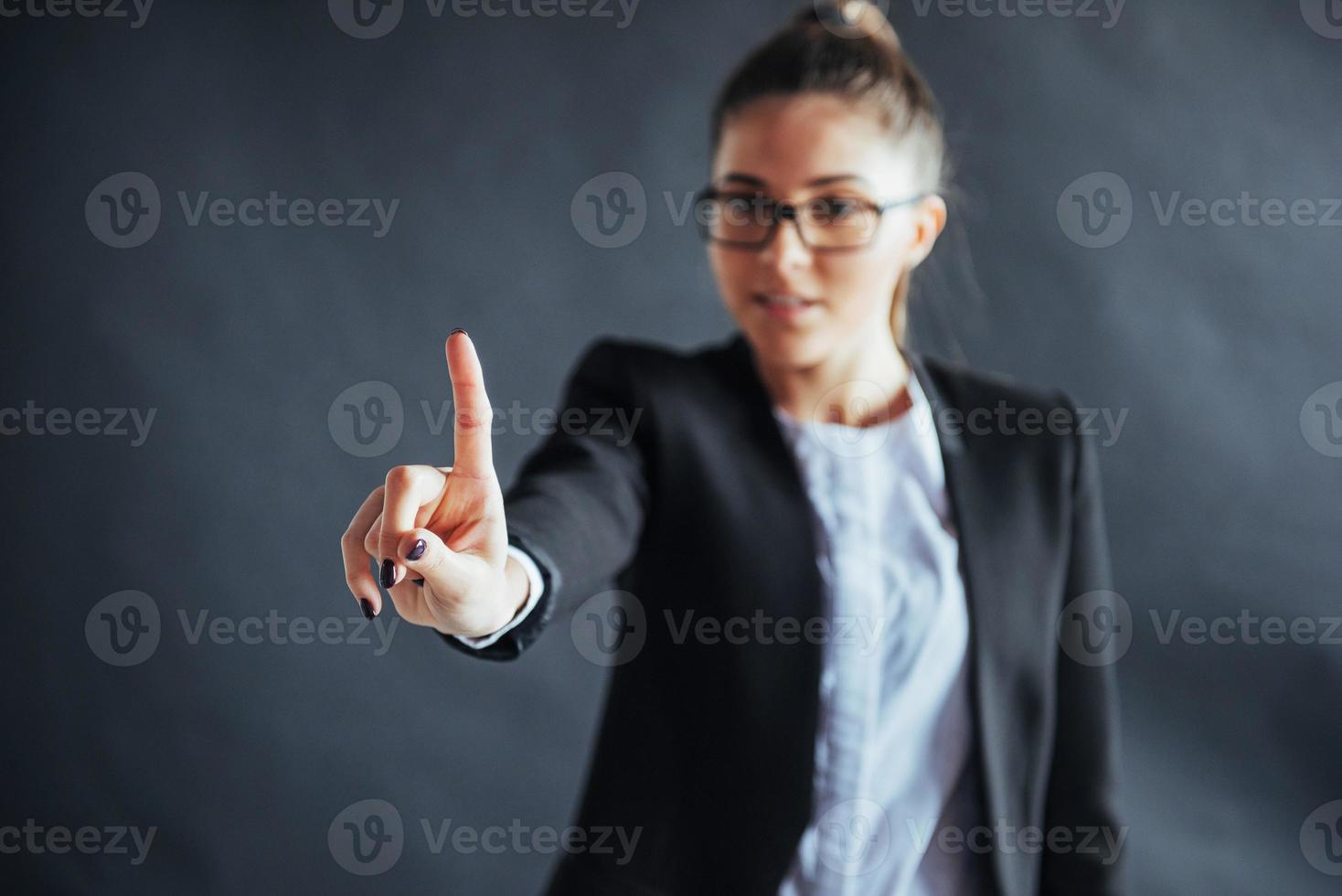 Happy business woman shows finger up, standing on a black background in the studio, friendly, smiling, focus on hand. photo