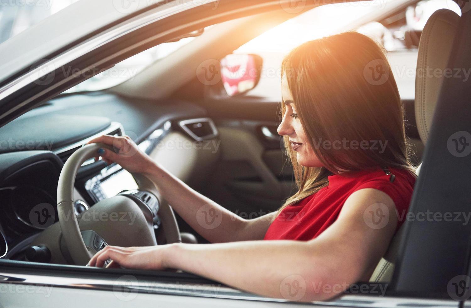 mujer en auto interior mantiene la rueda girando sonriendo mirando a los pasajeros en el asiento trasero idea taxista contra los rayos del atardecer luz brillo cielo concepto de vehículo de examen - segundo hogar la niña foto