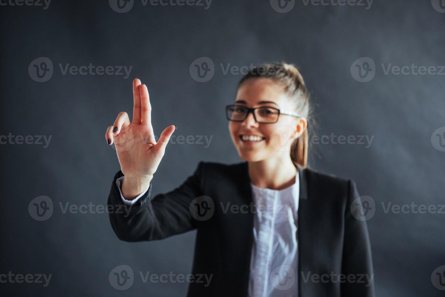 Happy business woman shows finger up, standing on a black background in the studio, friendly, smiling, focus on hand. photo