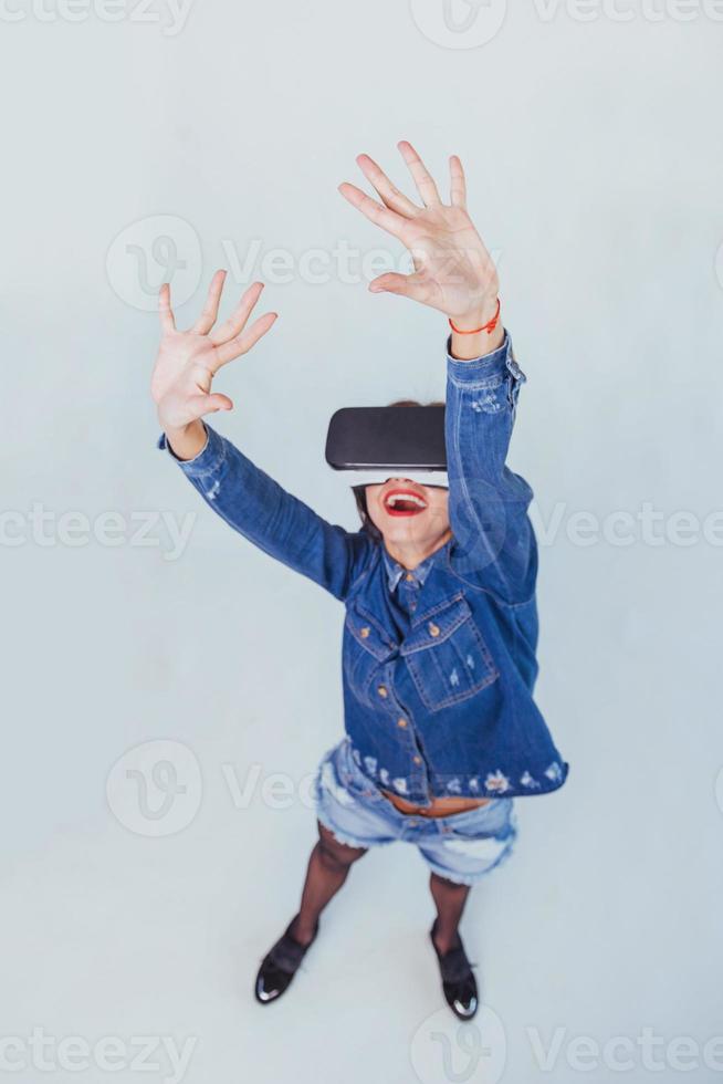 brunette beautiful woman posing in the studio, wearing jeans wear, using VR-glasses virtual reality headsets photo