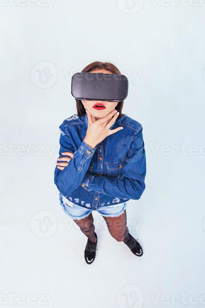 brunette beautiful woman posing in the studio, wearing jeans wear, using VR-glasses virtual reality headsets photo