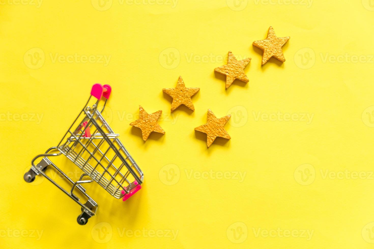 Simply flat lay design small supermarket grocery push cart for shopping with wheels and 5 gold stars rating isolated on yellow background. Retail consumer buying online assessment and review concept. photo
