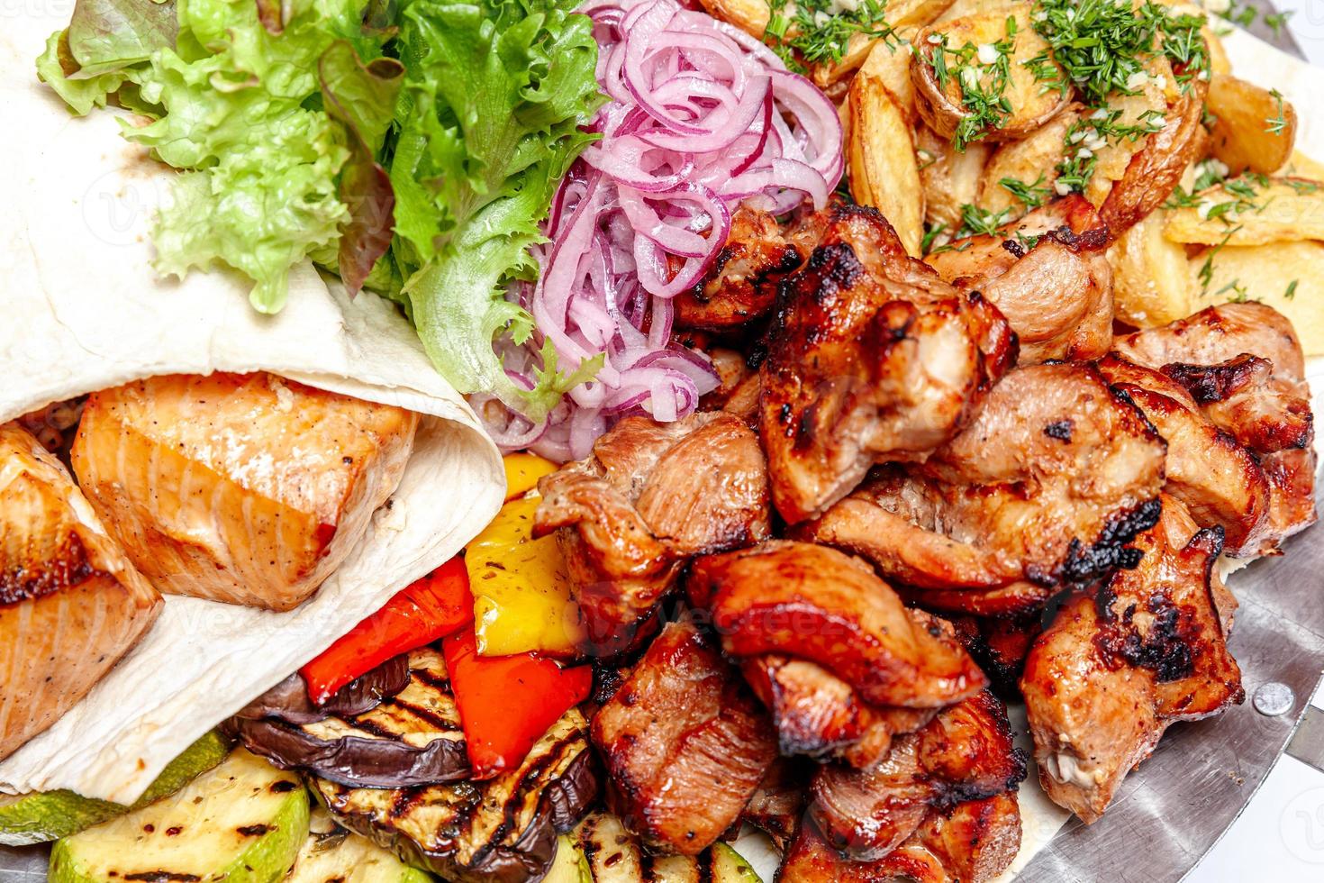 Mixed grill meat fried vegetables and grilled salmon fish fillets decoration in warm dish. Assorted delicious grilled kebab served with herbs on platter. Restaurant menu barbecue plate Bbq party meal photo