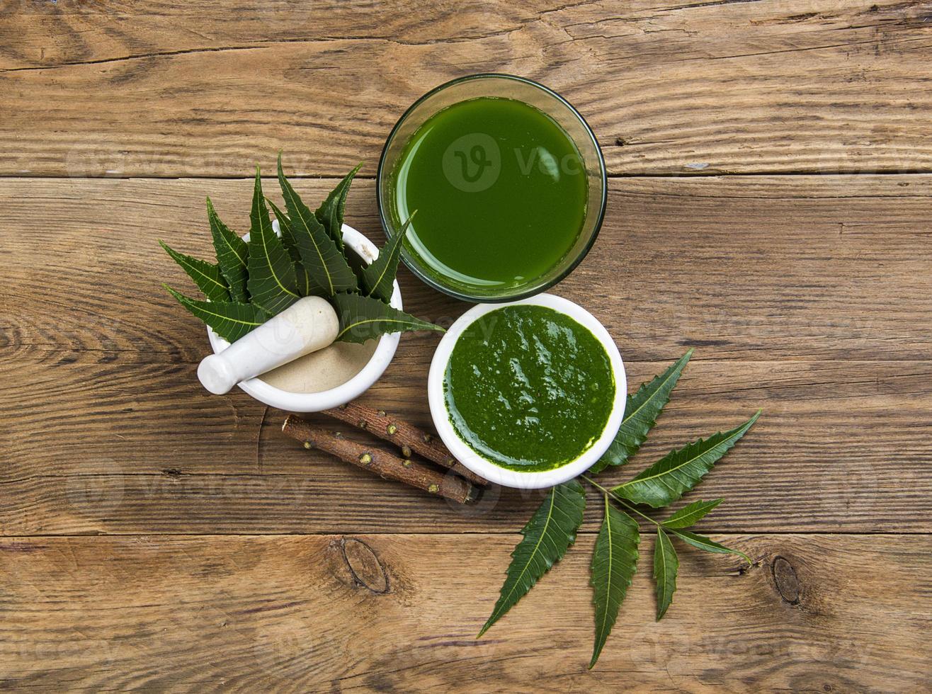 Medicinal Neem leaves in mortar and pestle with neem paste, juice and twigs on wooden background photo
