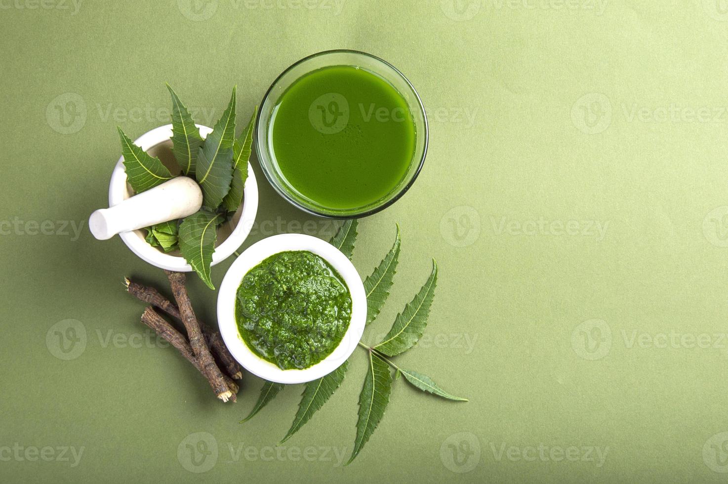 Medicinal Neem leaves in mortar and pestle with neem paste, juice and twigs on green background photo