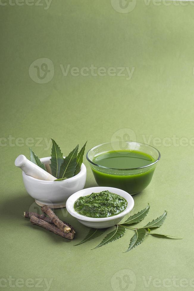 hojas medicinales de neem en mortero y mortero con pasta de neem, jugo y ramitas sobre fondo verde foto