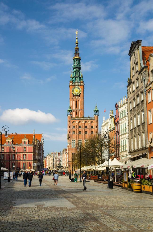 gdansk, polonia, 17 de abril de 2018, la gente camina por dluga long market street dlugi targ square en el antiguo centro histórico cerca del ayuntamiento con la torre del reloj, hermosos edificios típicos de casas coloridas foto