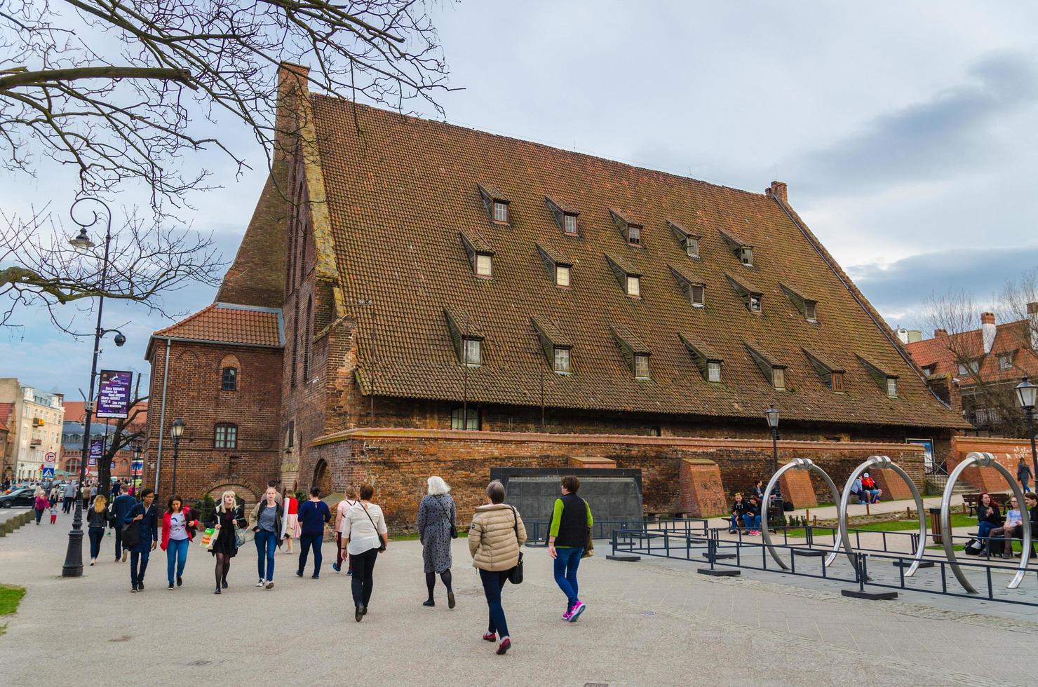 Gdansk, Poland, April 15, 2018 People walk near large water mill Wielki Mlyn with tiled roof near Radunia Canal channel in historic old town photo