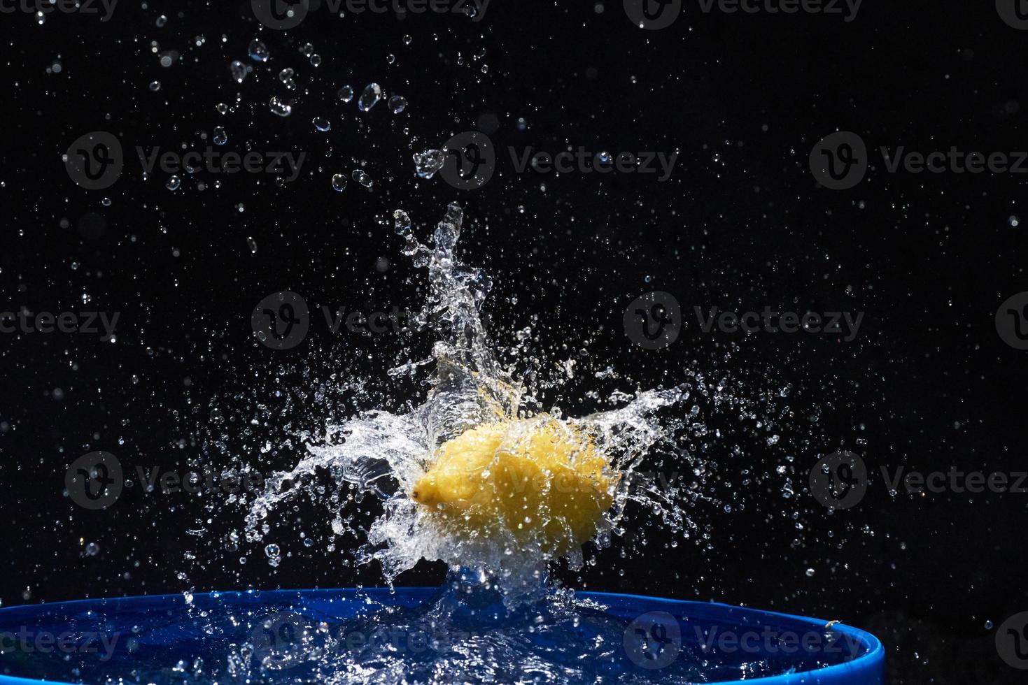 limón amarillo cayendo en el agua azul sobre un fondo negro foto