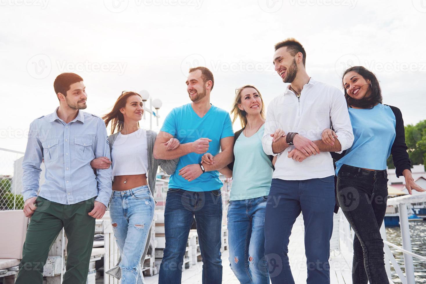 Portrait of a group of young people sitting on the edge of the pier, outdoors in nature. Friends enjoying a game on the lake. photo