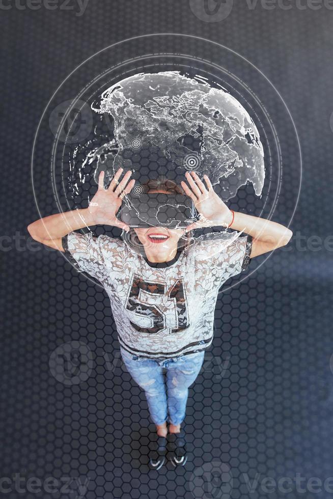 Young beautiful girl gets positive emotions using virtual reality goggles. The woman plays a game using augmented reality. Virtual world map photo