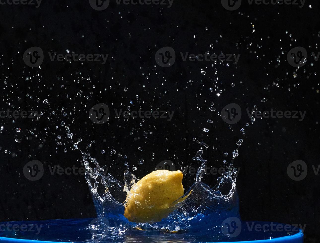 limón amarillo cayendo en el agua azul sobre un fondo negro foto