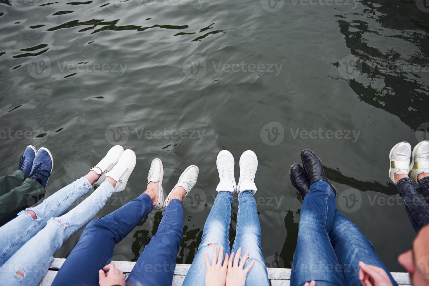 Young people friends sitting on the river bridge, lifestyle, feet over blue water photo