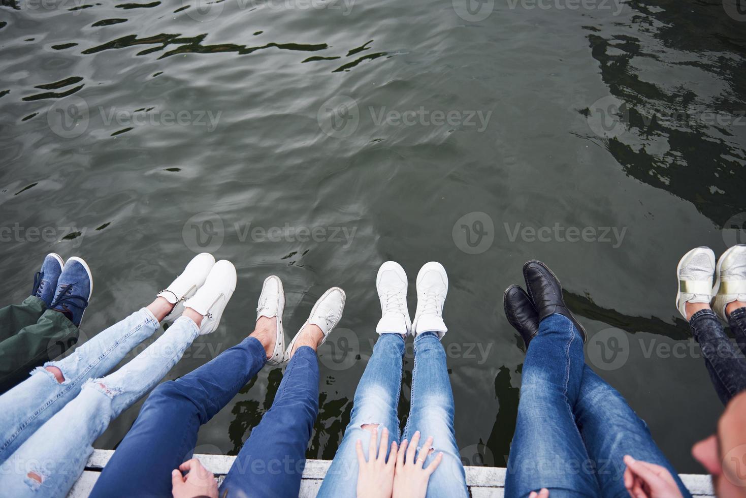 jóvenes amigos sentados en el puente del río, estilo de vida, pies sobre el agua azul foto