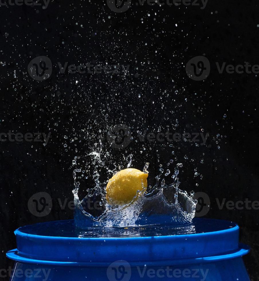 limón amarillo cayendo en el agua azul sobre un fondo negro foto