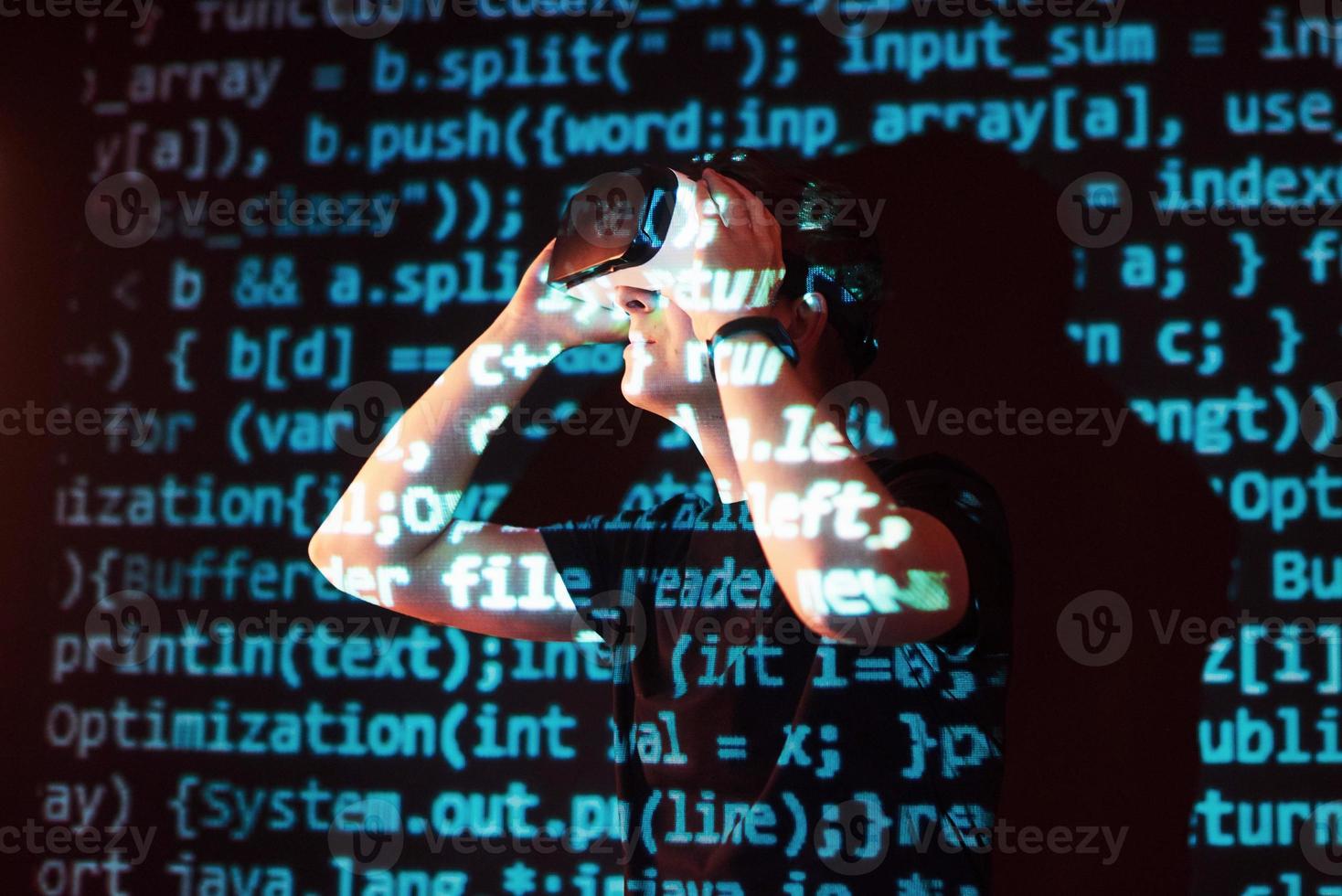 Double exposure of a caucasian man and Virtual reality headset is presumably a gamer or a hacker cracking the code into a secure network or server, with lines of code photo