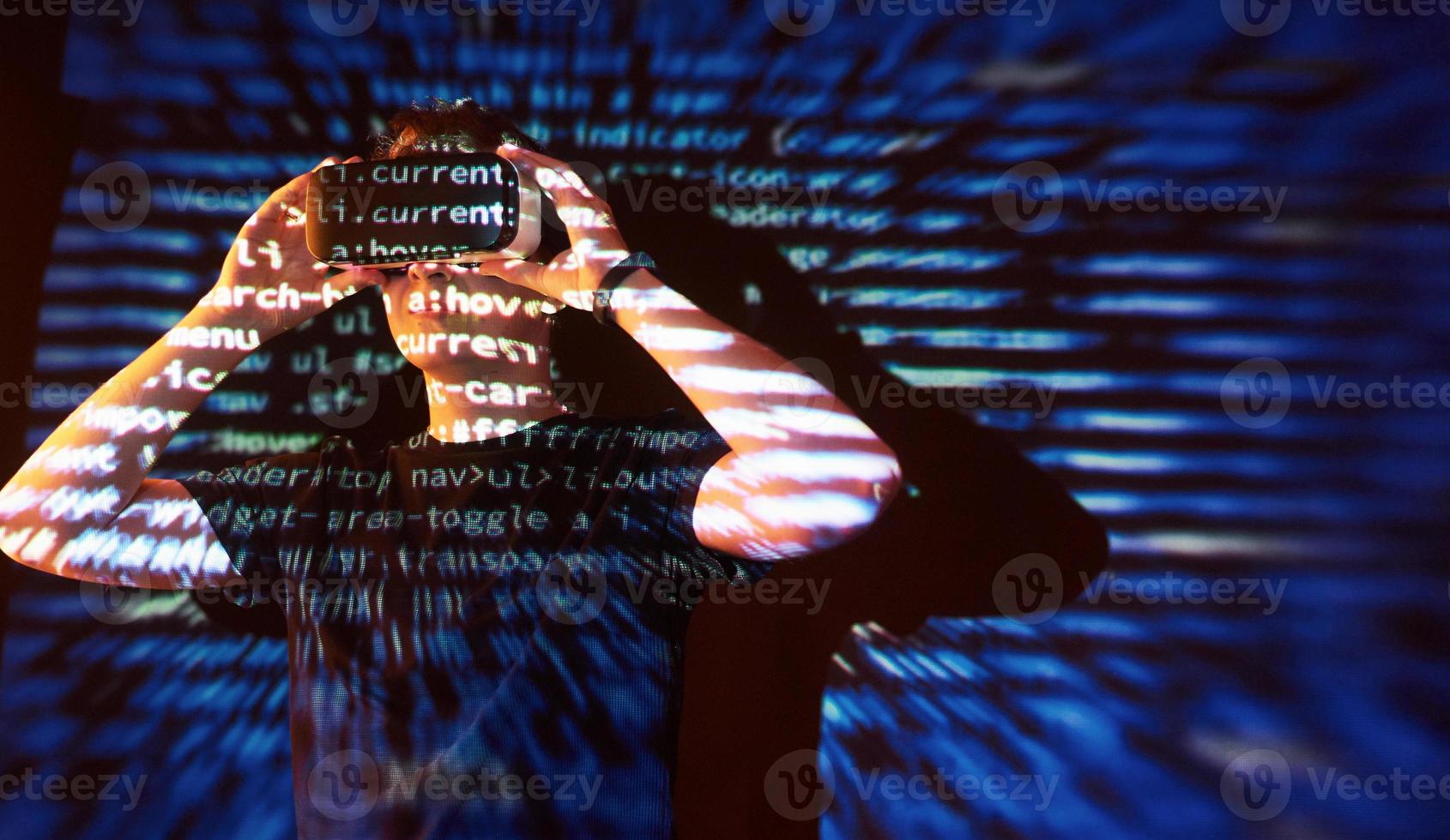 Double exposure of a caucasian man and Virtual reality headset is presumably a gamer or a hacker cracking the code into a secure network or server, with lines of code photo