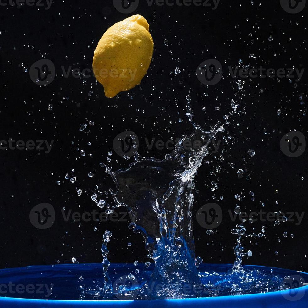 jugoso limón amarillo cae en agua sobre un fondo negro foto