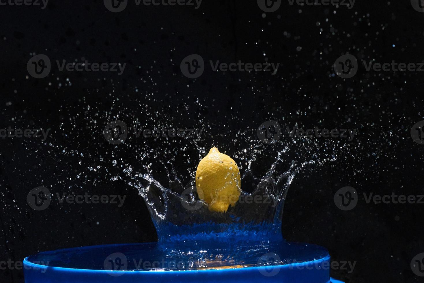 Yellow lemon falling in the blue water on a black background photo