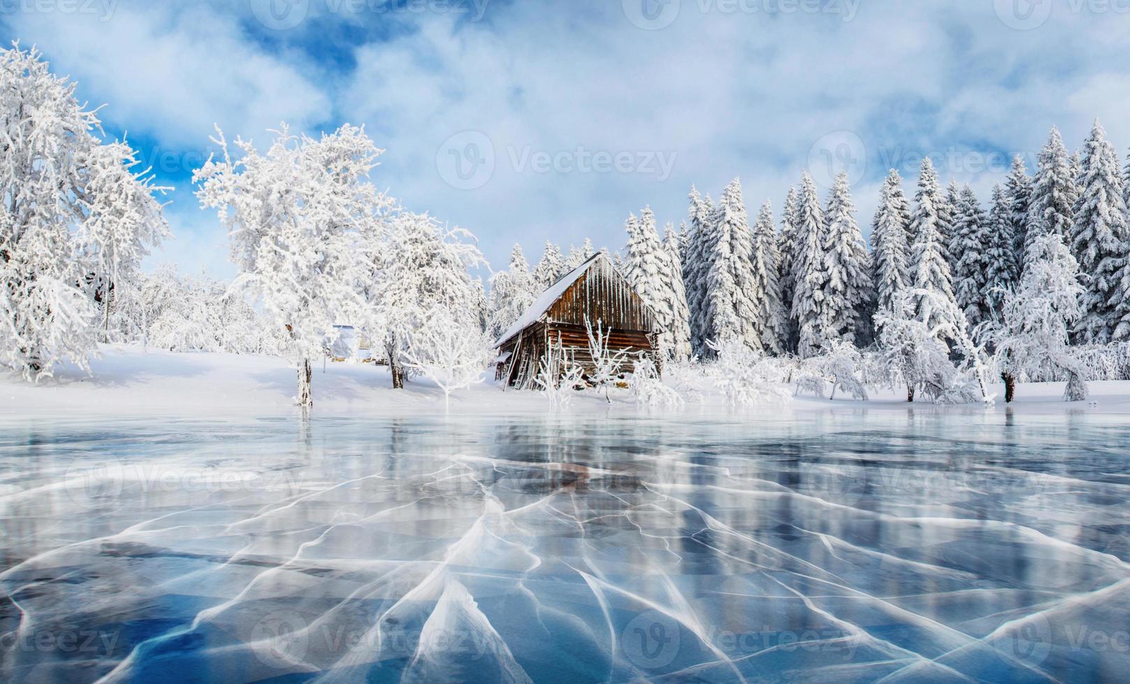 hielo azul y grietas en la superficie del hielo. lago congelado bajo un cielo azul en invierno. cabaña en las montañas. niebla misteriosa. montes de Cárpatos. ucrania, europa foto