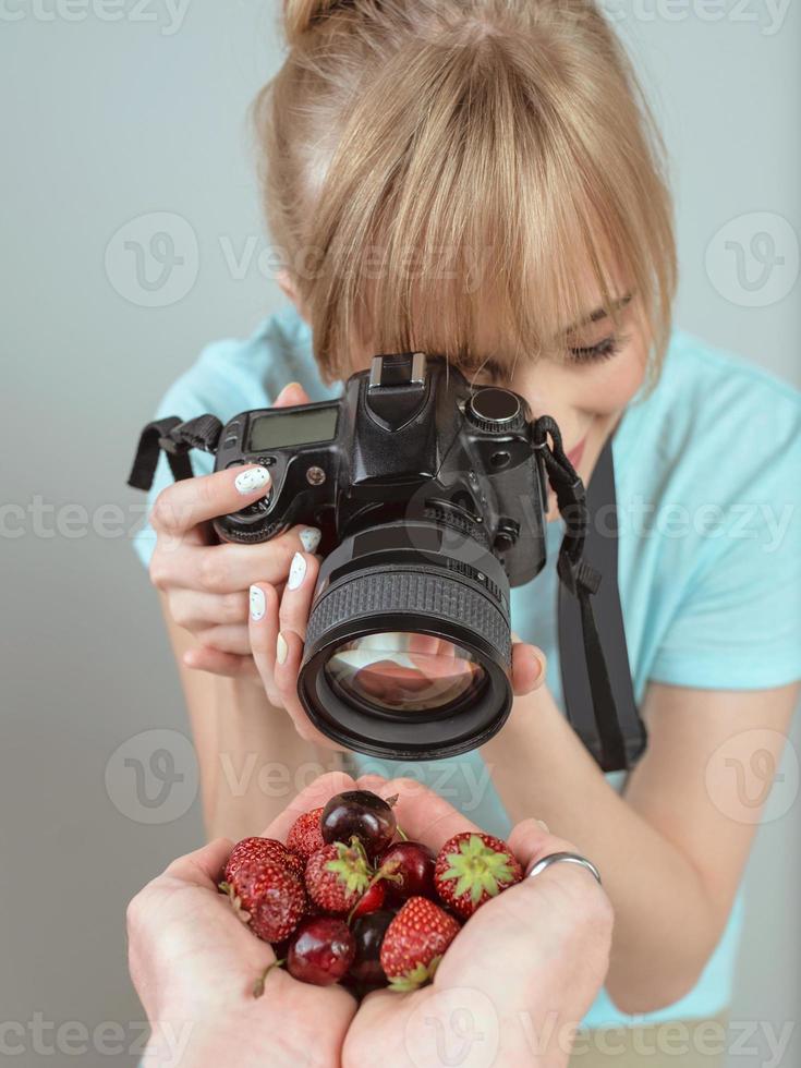 joven fotógrafa disparando con cámara digital fresas y cerezas en las manos. primer plano, tiro, hobby, comida, concepto de profesión foto