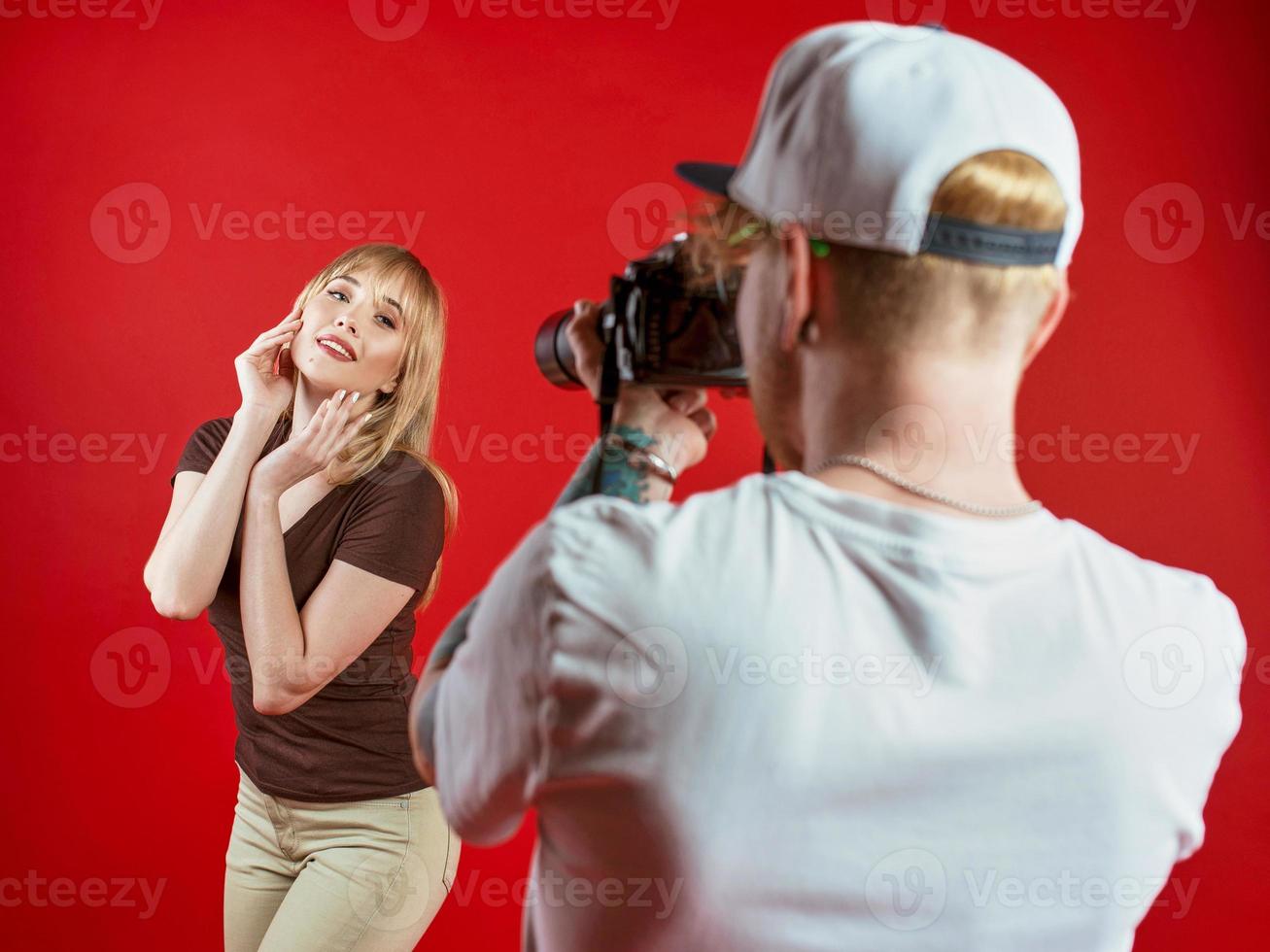 modelo posando para fotógrafo en estudio sobre fondo rojo. profesional, educación, concepto de tecnología. foto