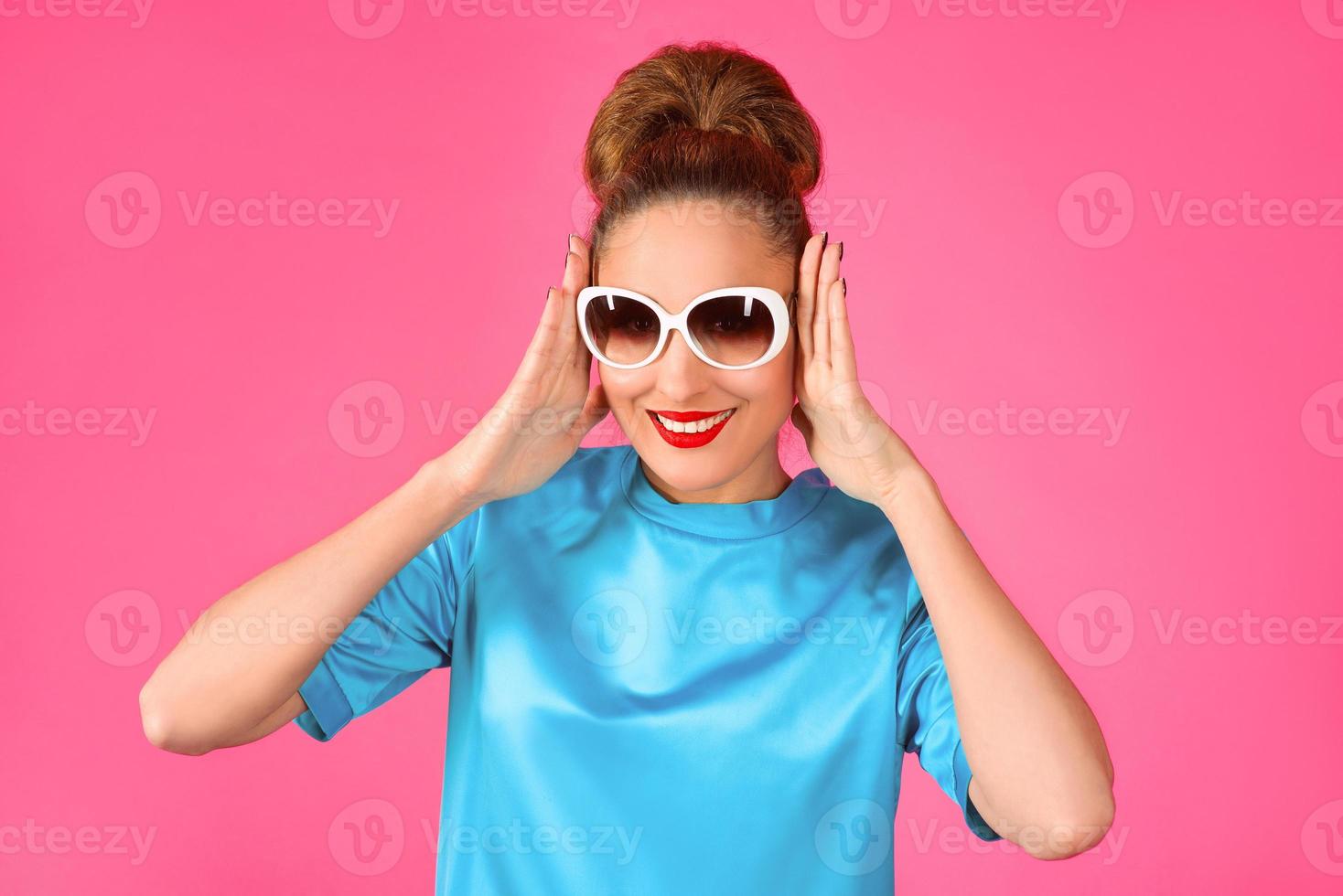 portrait of young beautiful woman in blue silk dress and white sunglasses ot the pink background photo