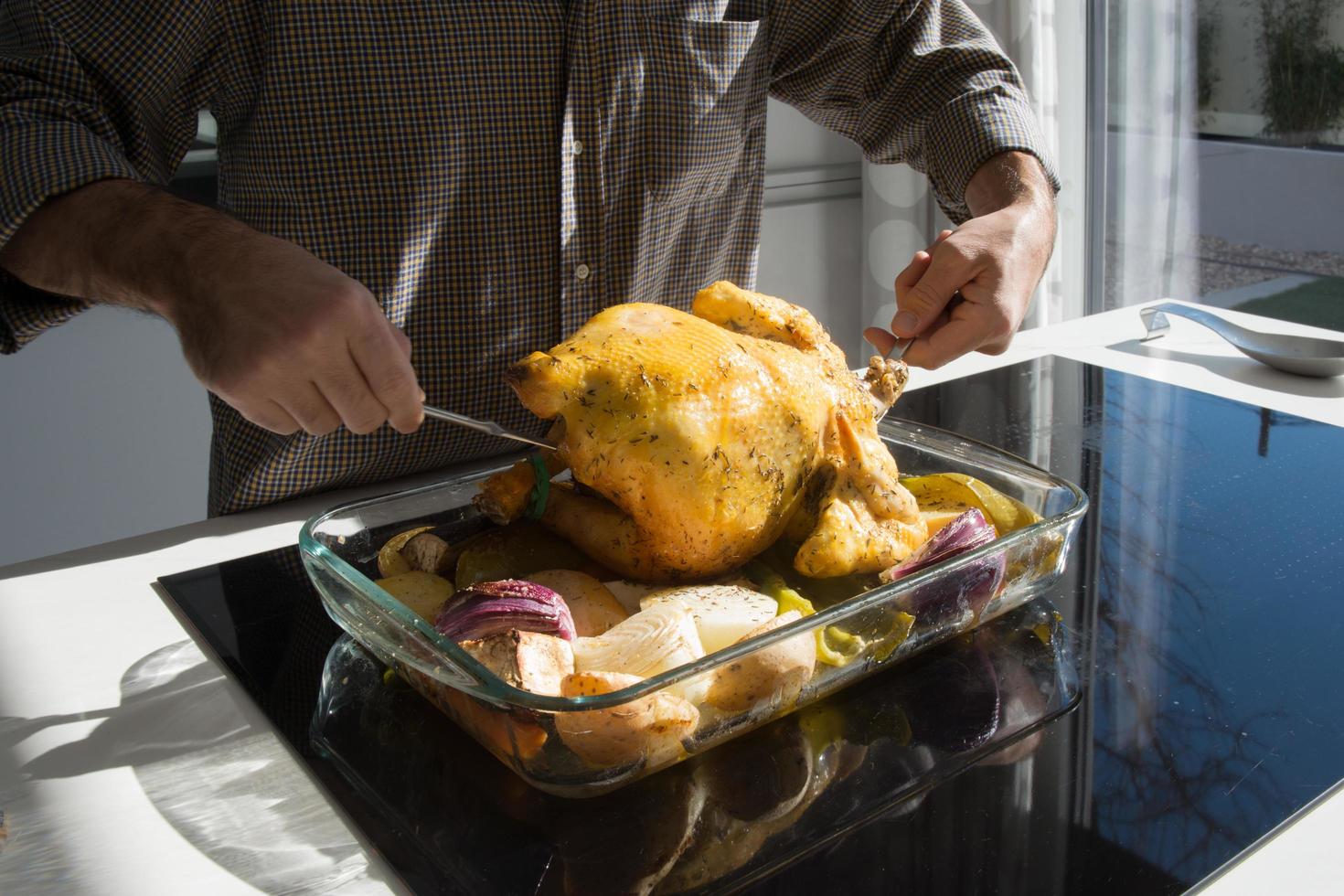 hombre irreconocible preparando un jugoso pollo al horno con verduras. foto