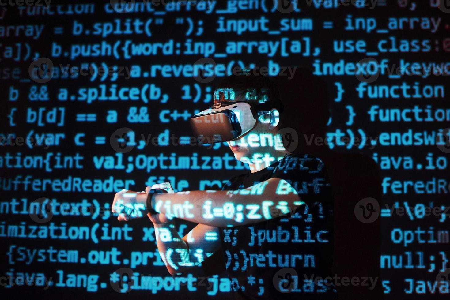 Double exposure of a caucasian man and Virtual reality headset is presumably a gamer or a hacker cracking the code into a secure network or server, with lines of code photo