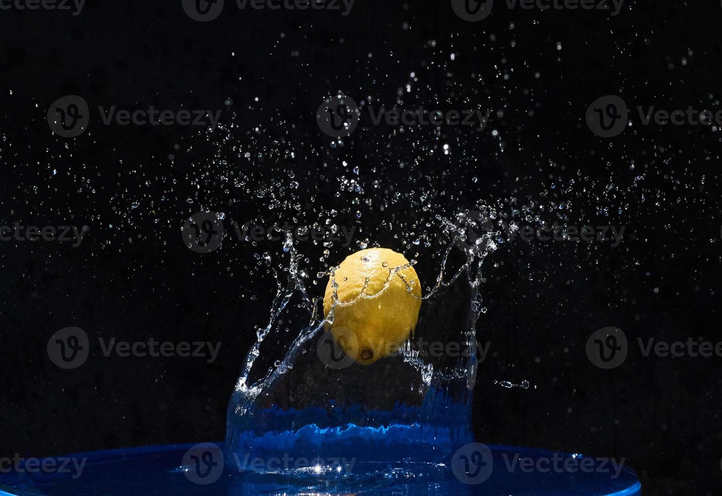 limón amarillo cayendo en el agua azul sobre un fondo negro foto