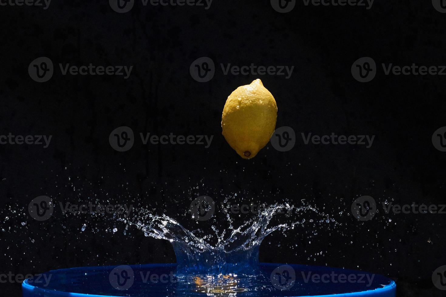 Juicy yellow lemon falls in water on a black background photo