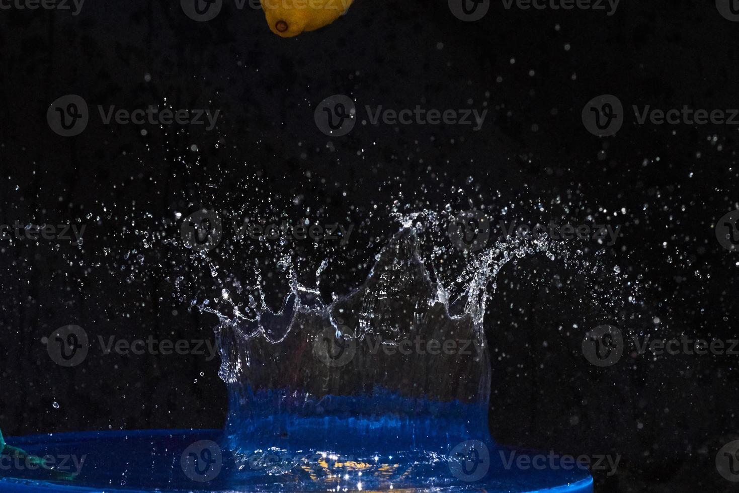 Yellow lemon falling in the blue water on a black background photo