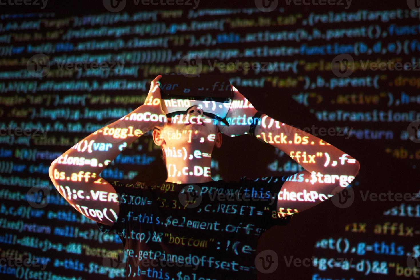 Double exposure of a caucasian man and Virtual reality headset is presumably a gamer or a hacker cracking the code into a secure network or server, with lines of code photo