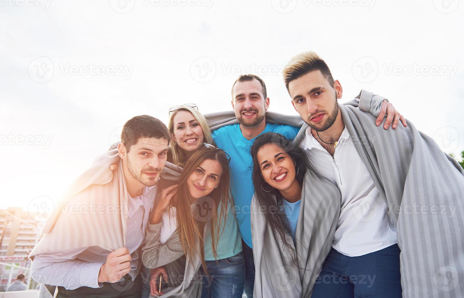 Portrait of a group of young people sitting on the edge of the pier, outdoors in nature. Friends enjoying a game on the lake. photo