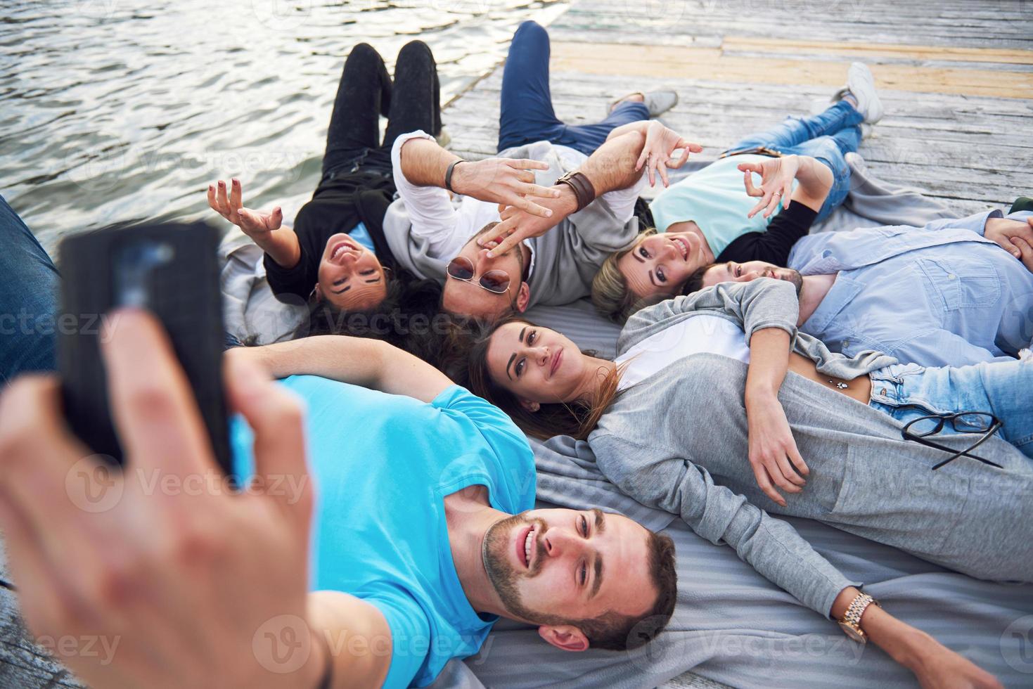 retrato de jóvenes amigos felices en el muelle del lago. mientras disfruta del día y hace selfie. foto