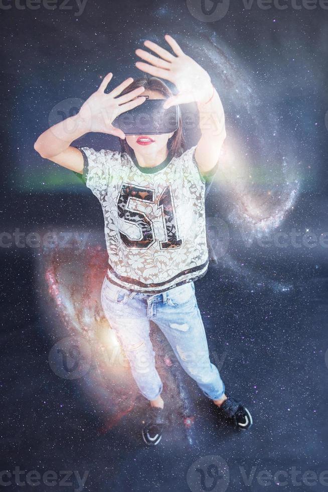 Young beautiful girl gets positive emotions using virtual reality goggles. A woman examines star via Augmented Reality. photo