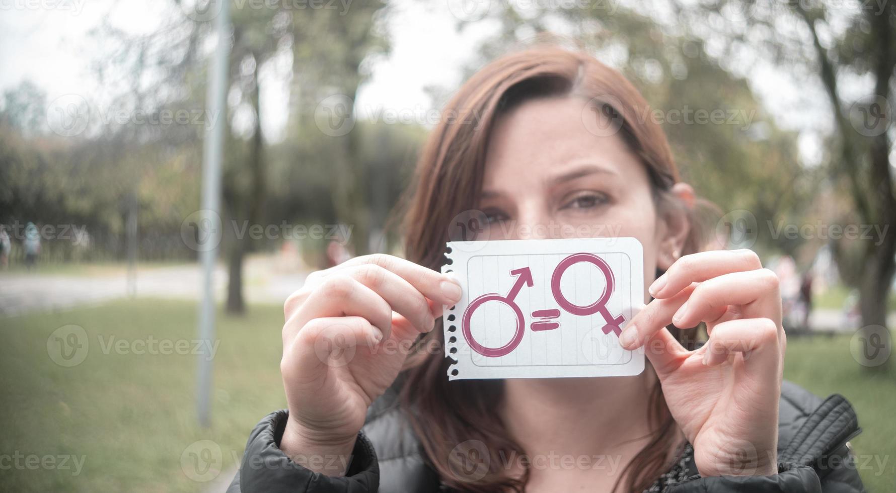 Beautiful Hispanic woman in the middle of a park holding in her hand a paper with the message of equality with the icons of man and woman photo