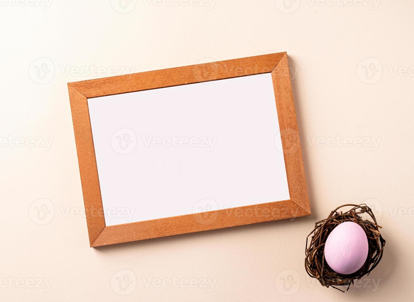 Wooden frame with colored easter egg flat lay on beige background photo