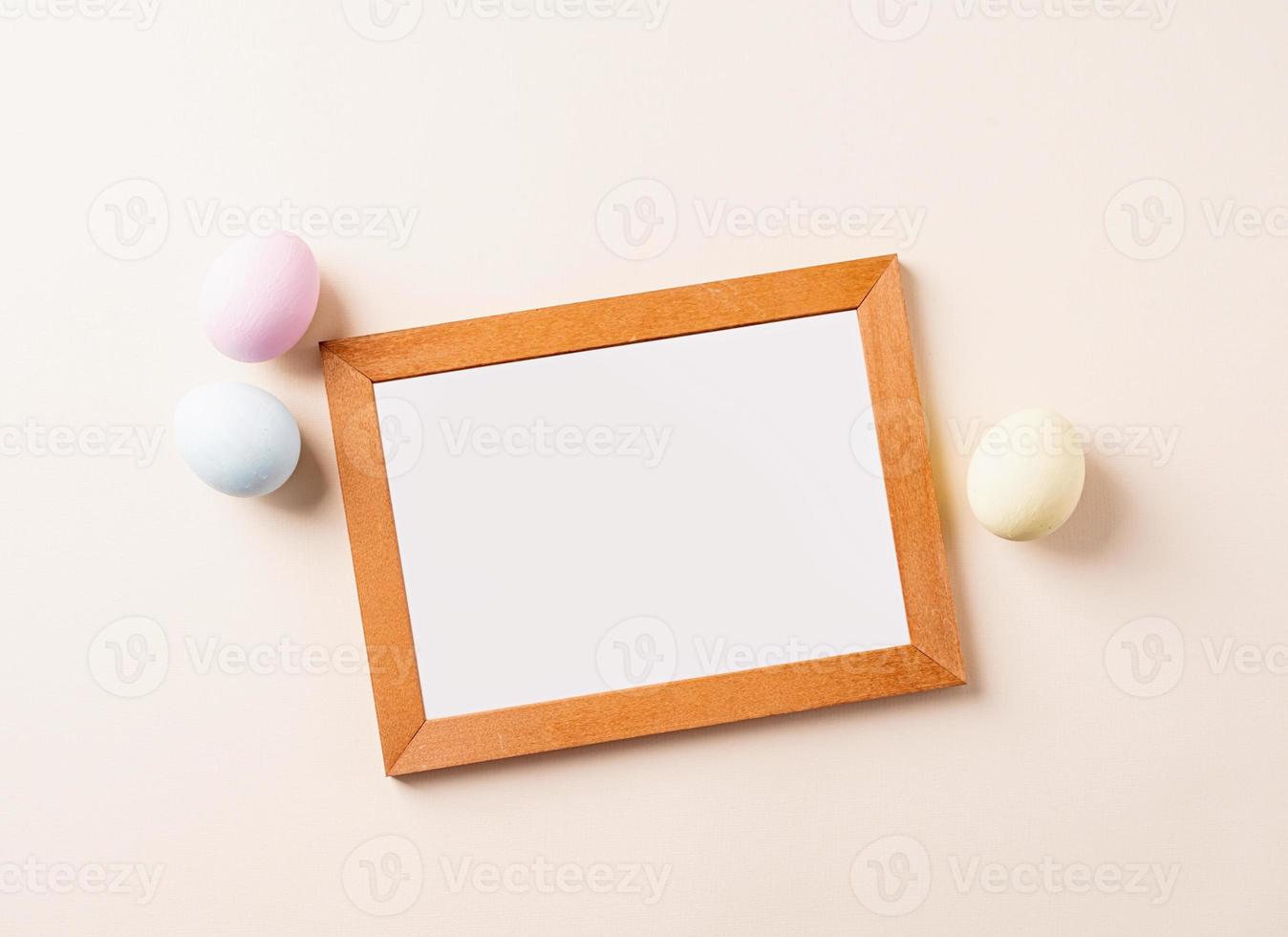 Wooden frame with colorful easter eggs flat lay on beige background photo