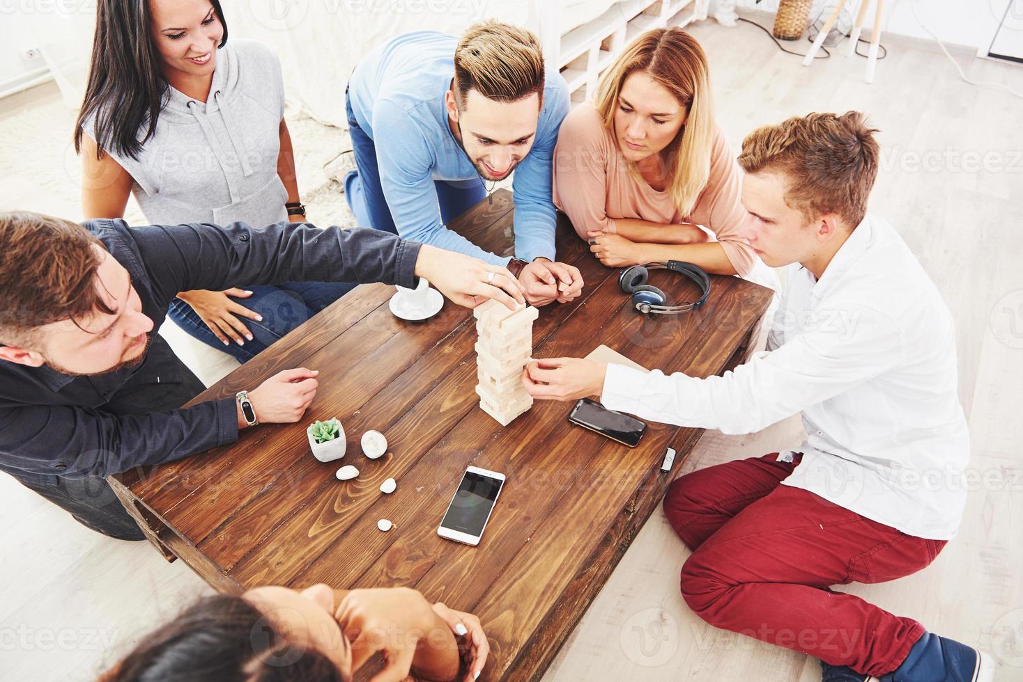 grupo de amigos creativos sentados en la mesa de madera. gente divirtiéndose mientras juega al juego de mesa. foto