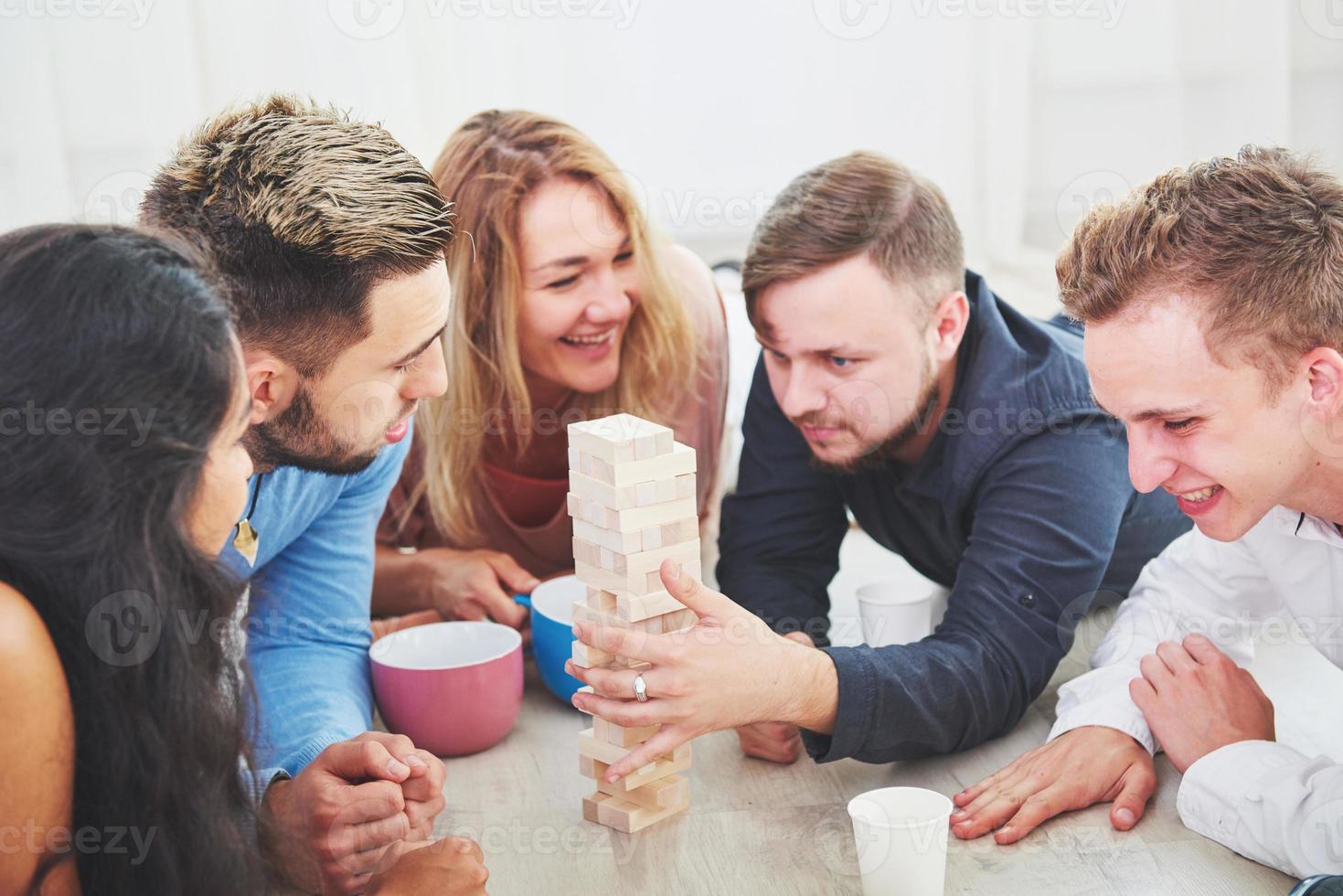 Group of creative friends sitting at wooden table. People having fun while playing board game photo