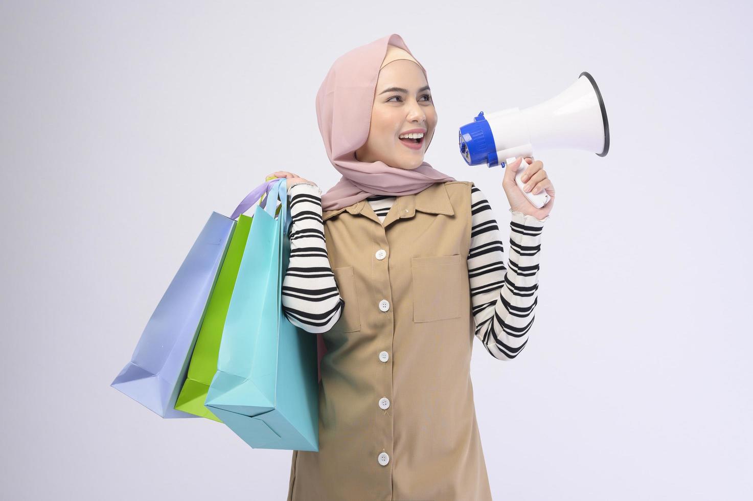 Young beautiful muslim woman in suit holding colorful shopping bags over white background studio photo