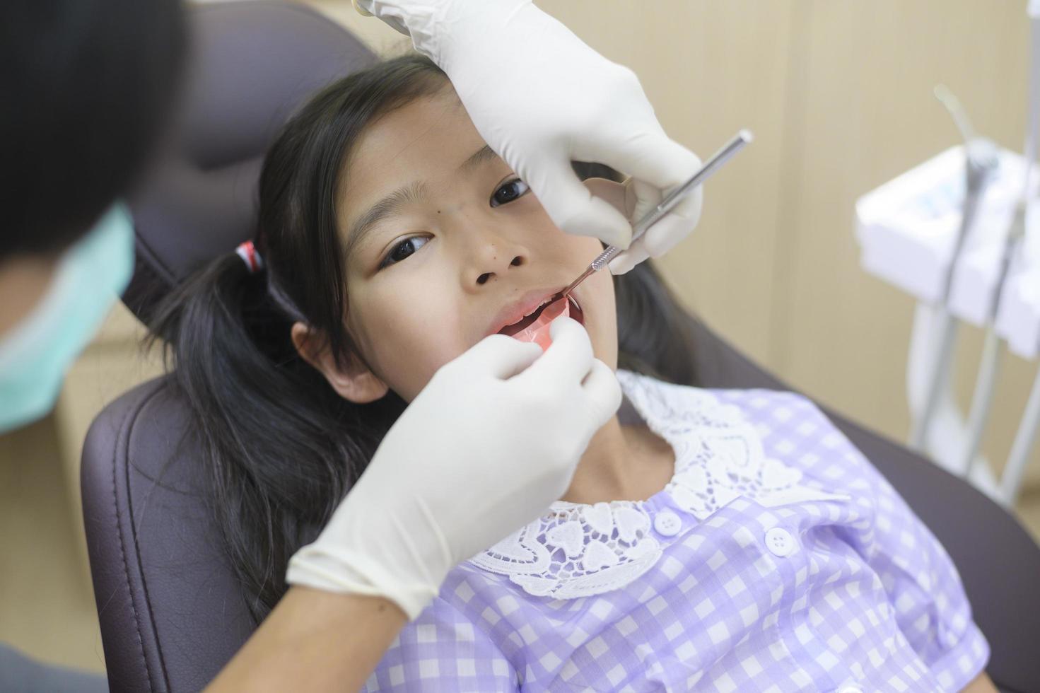 una niña linda con los dientes examinados por un dentista en una clínica dental, un chequeo dental y un concepto de dientes sanos foto