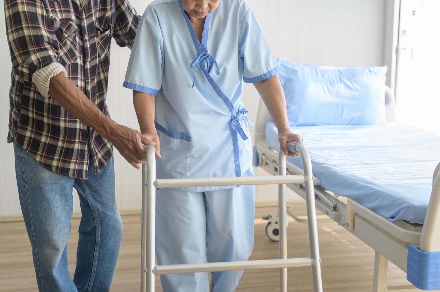 Senior man helping cancer patient woman wearing head scarf with walker at hospital, health care and medical concept photo