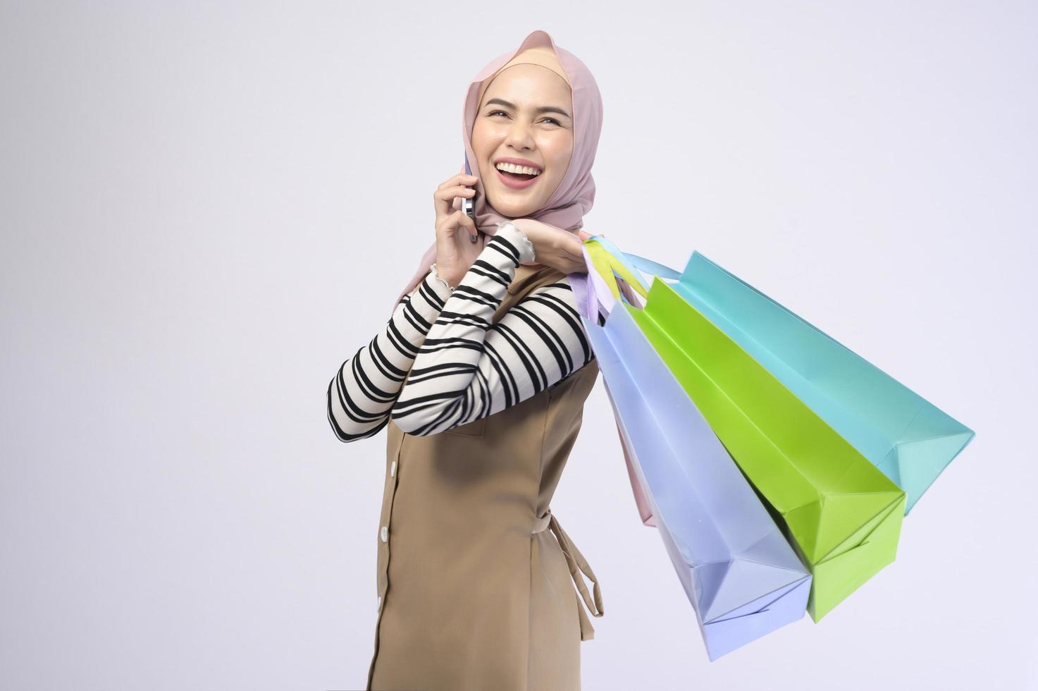 Young beautiful muslim woman in suit holding colorful shopping bags over white background studio photo