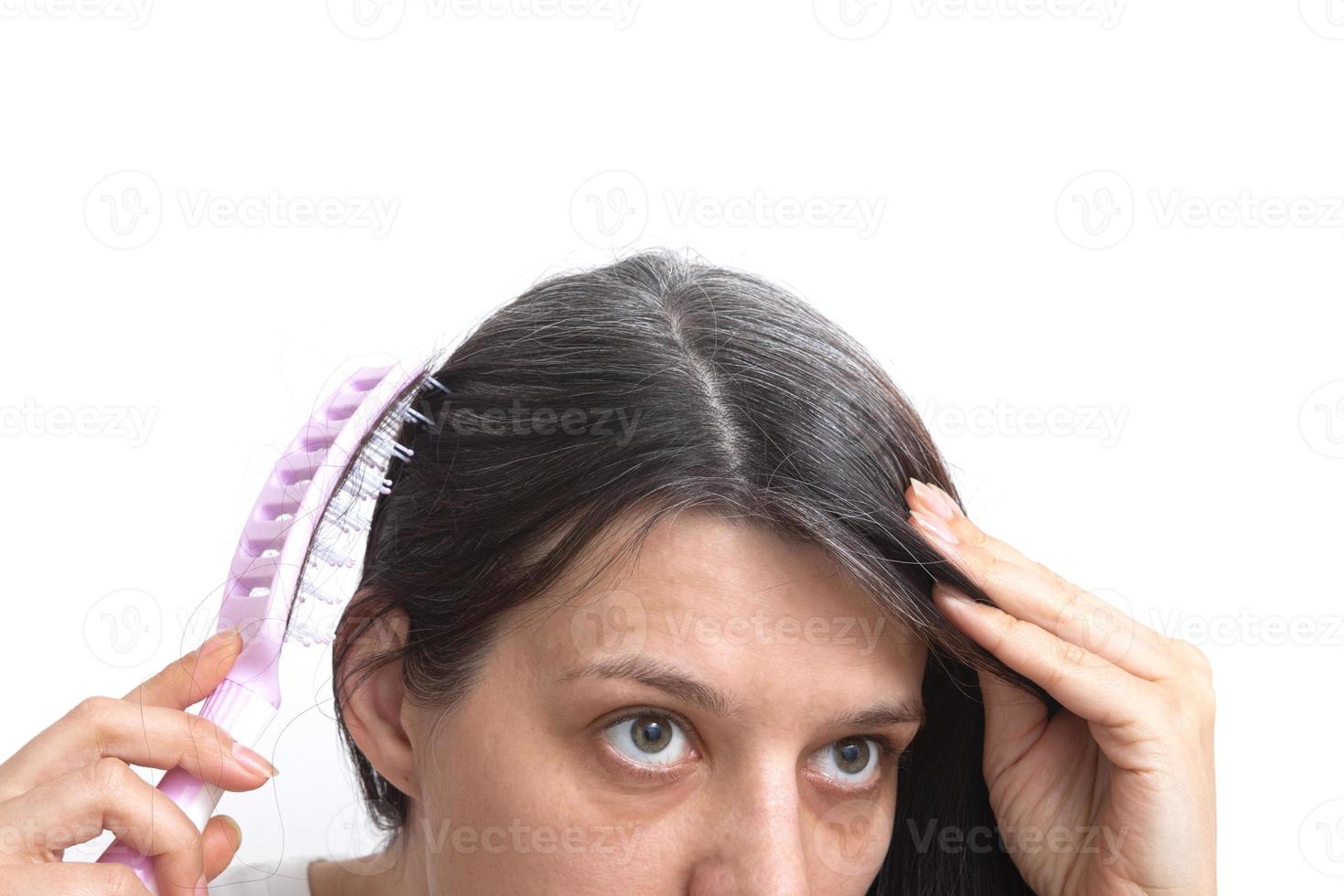 A young woman with a comb looks at her gray hair in the mirror. The concept of early gray hair. photo