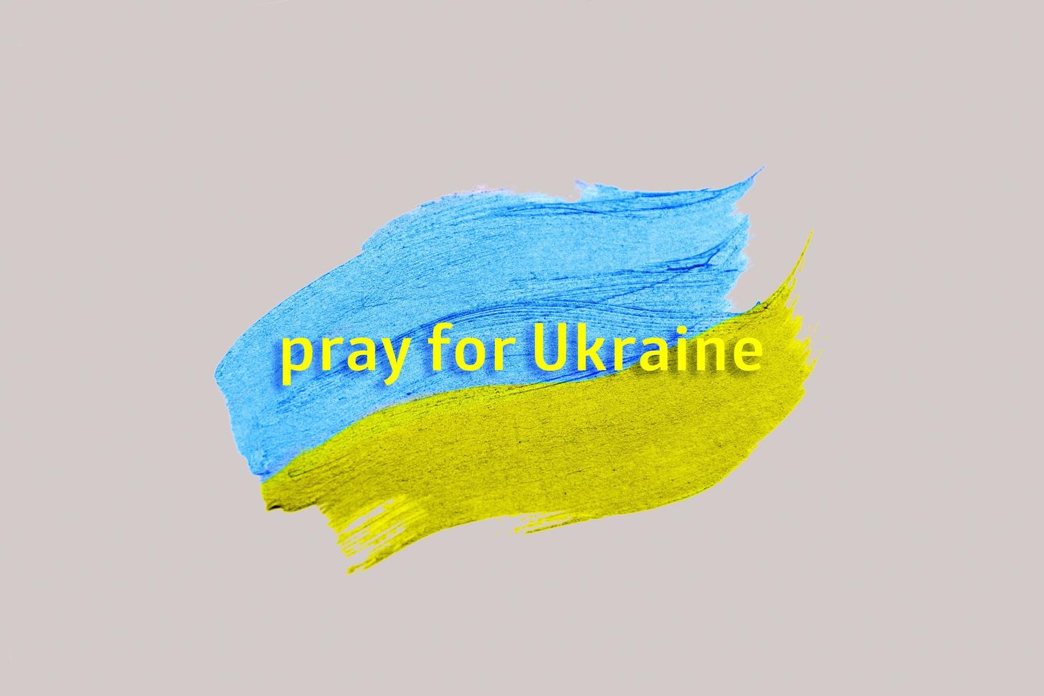 I pray for Ukraine inscription on the background of strokes of paint tinted in the color of the Ukrainian flag photo